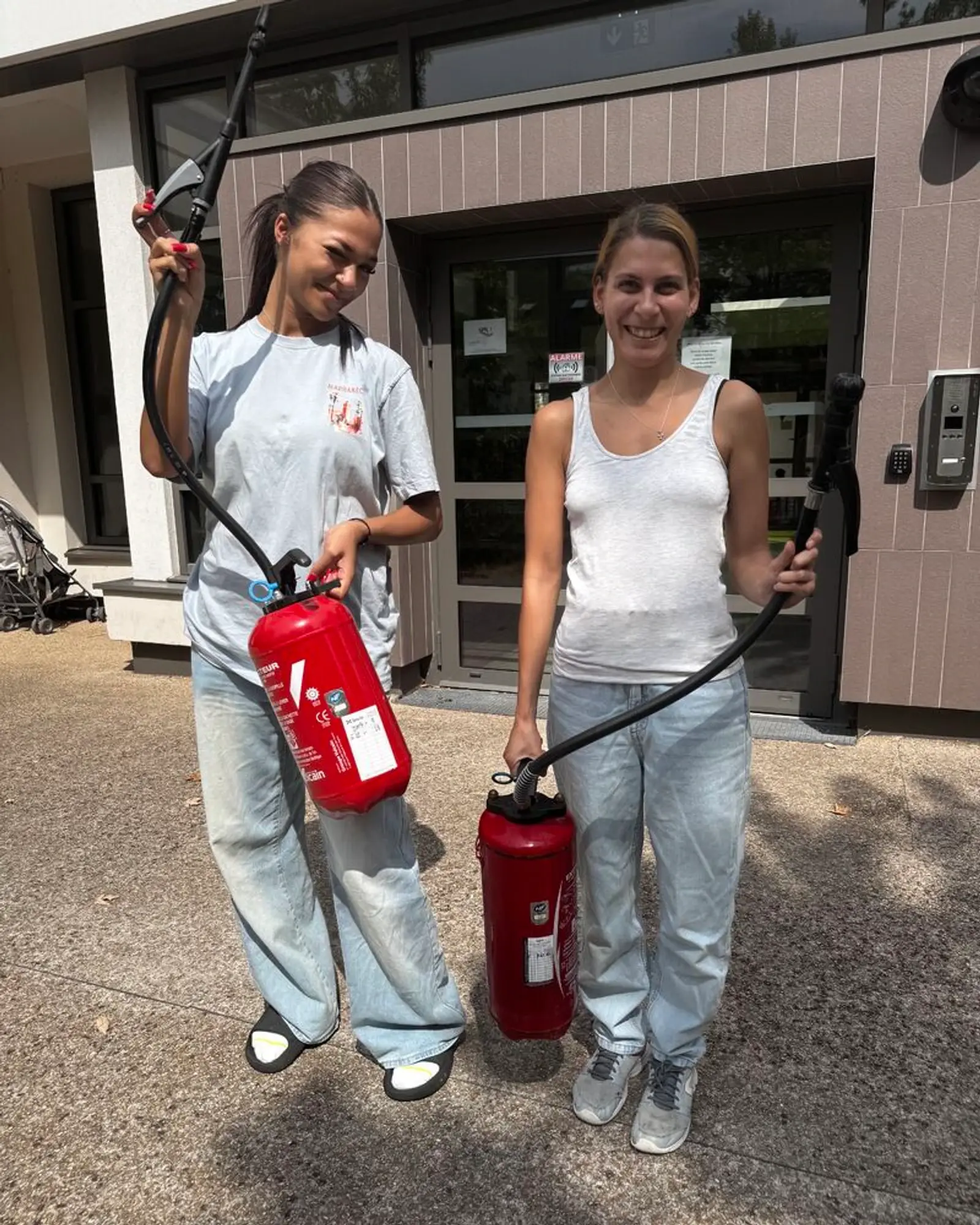 Deux stagiaires avec un extincteur devant l’entrée de la structure